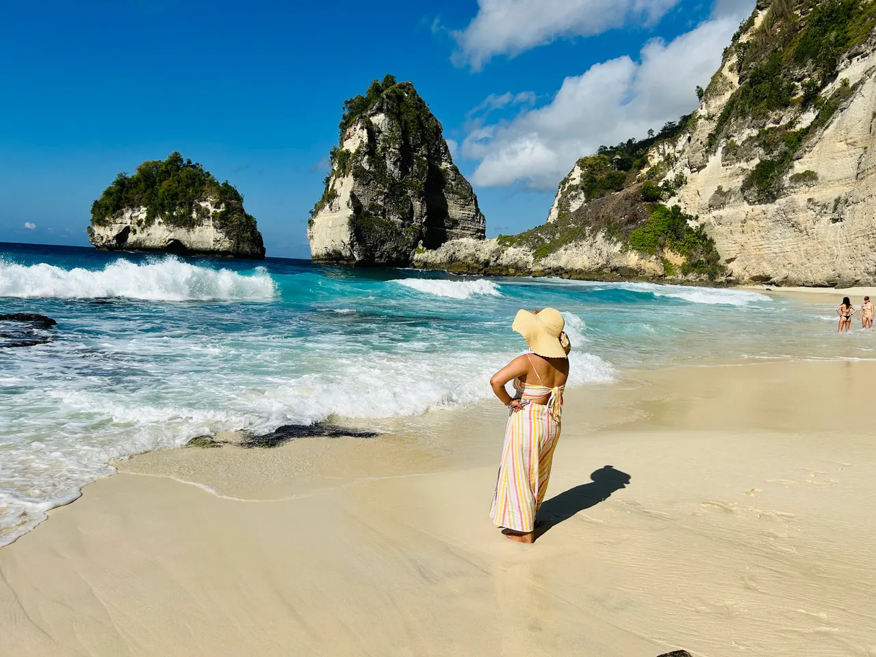 White sand, breaking surf and the limestone sea stacks of Diamond Beach, Nusa Penida, under blue sky.