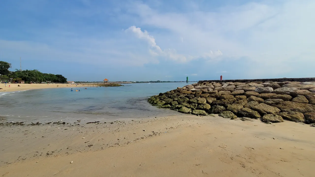 Calm shallow water and golden sand at Sanur Beach, Bali, under a bright blue sky.
