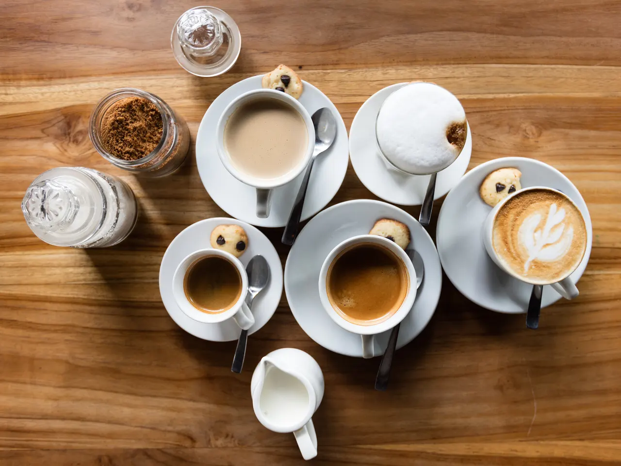 Overhead view of espresso, long black and a cappuccino with latte art on a wooden cafe table in Canggu, Bali.